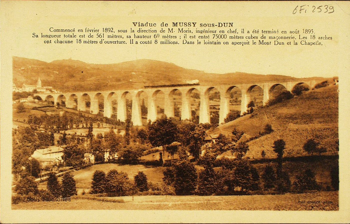 Viaduc de Mussy-sous-Dun. Commencé en février 1892, sous la direction de M. Moris, ingénieur en chef, il a été terminé en août 1895. Sa longueur totale est de 561 mètres, sa hauteur 60 mètres, il est entré 75000 mètres cubes de maçonnerie. Les 18 arches ont chacune 18 mètres d'ouverture. Il a coûté 8 millions. Dans le lointain on aperçoit le Mont Dun et la Chapelle.